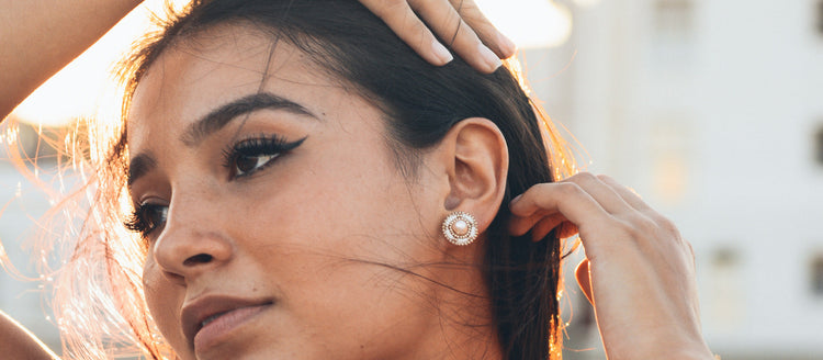 Indigenous Model Kinsale Wearing Cheyanne Symone’s Ivory Classic Freshwater Pearl Earrings with Champagne Gold Trim. Kinsale is brushing her windswept hair back and staring into the distance.