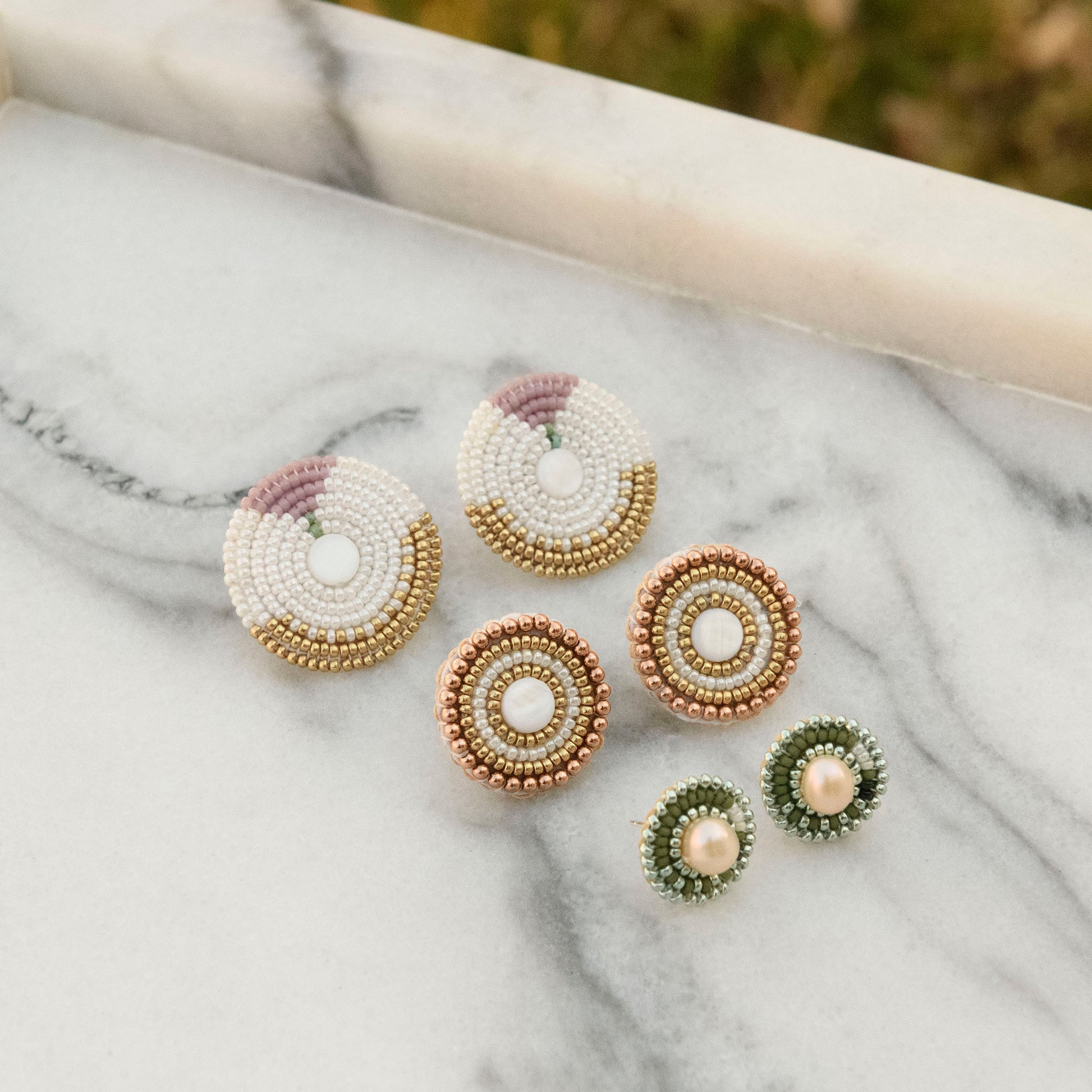 Cheyanne Symone’s In Bloom Statement Beaded Earrings, Rose Gold Pearl Earrings, and Sage Green Freshwater Pearl Stud Beaded Earrings on a Marble Background.